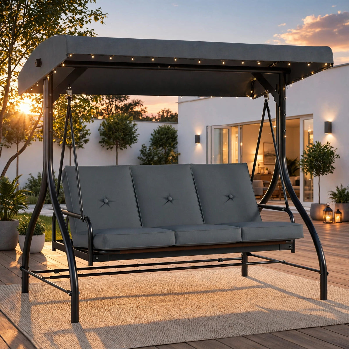 Charcoal gray 3-seater outdoor glider swing with canopy and fairy lights at golden hour sunset on modern patio