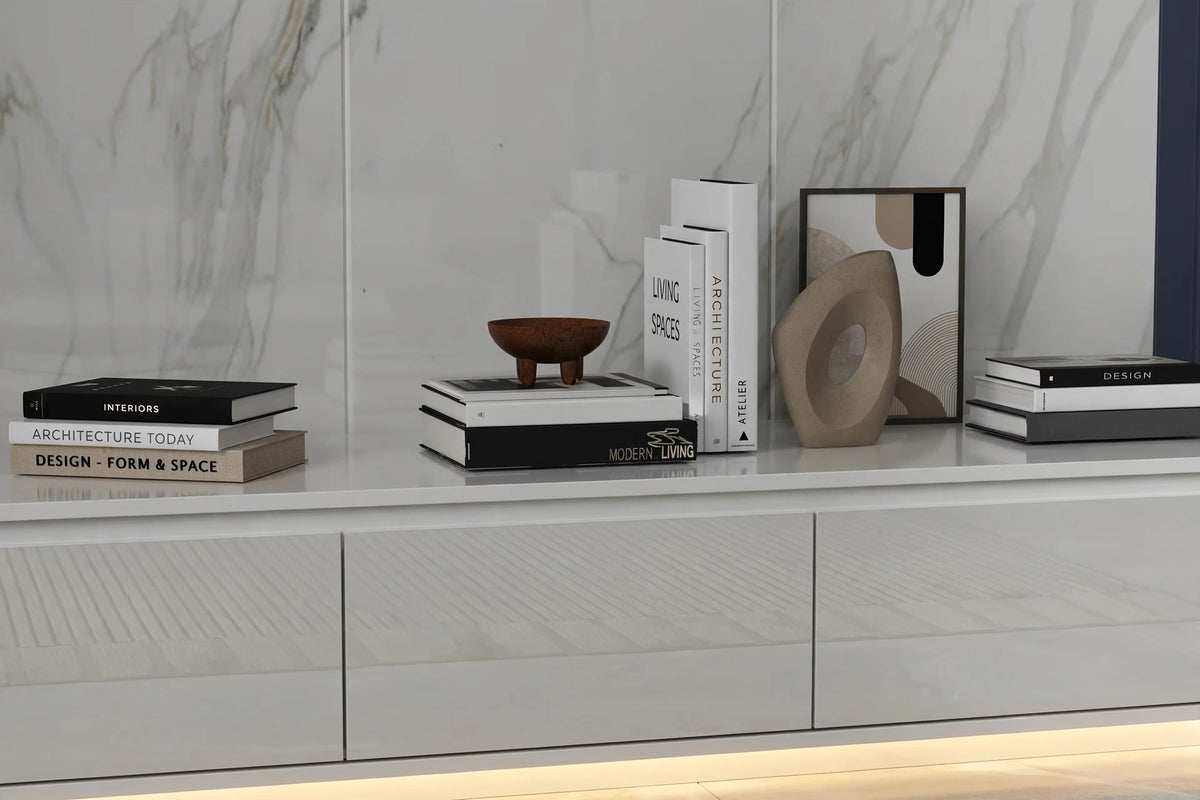 Close-up of floating TV console top surface styled with design books, wooden bowl and sculptural decor against marble backdrop