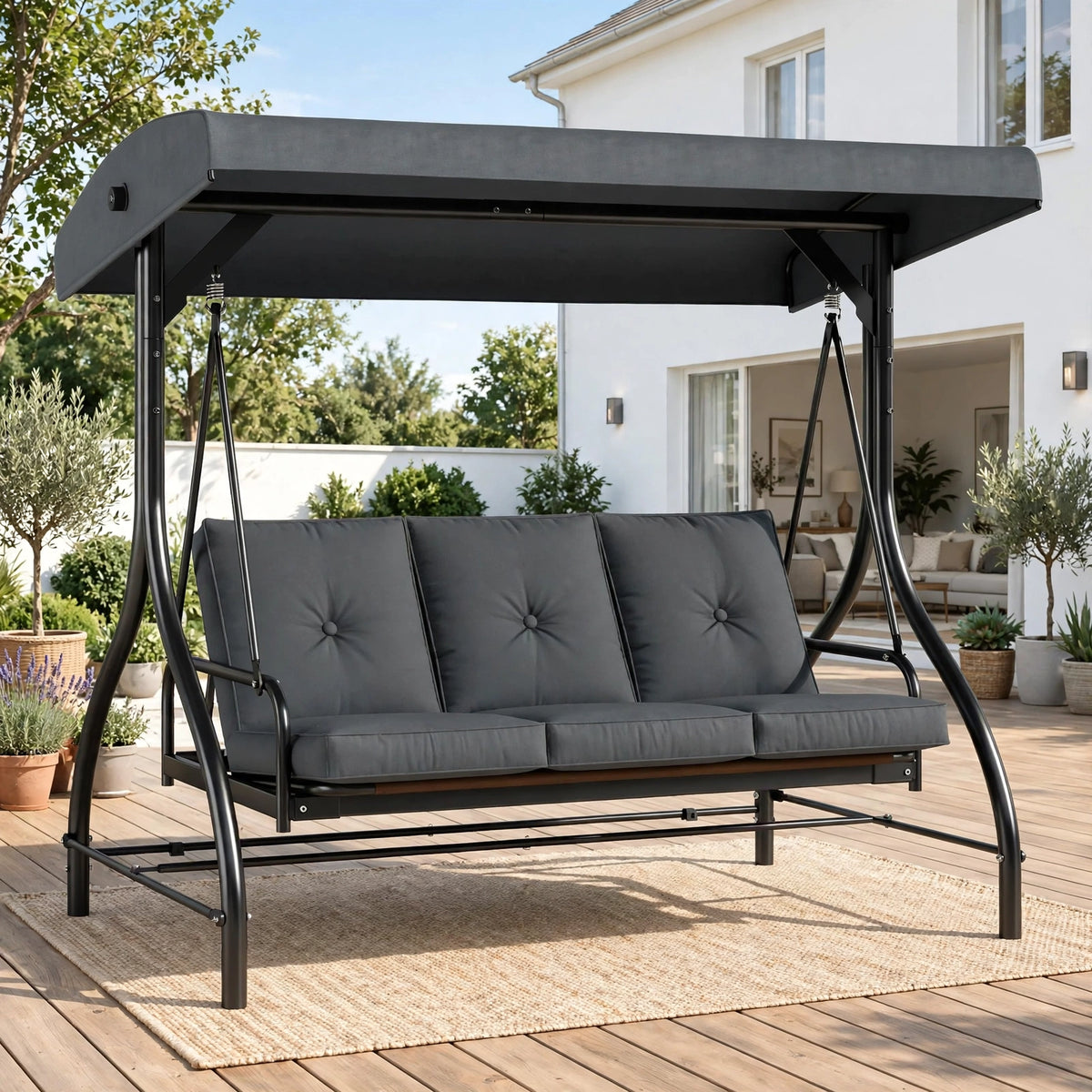 Charcoal gray 3-seater patio swing chair with adjustable canopy on sunny wooden deck with garden and house backdrop
